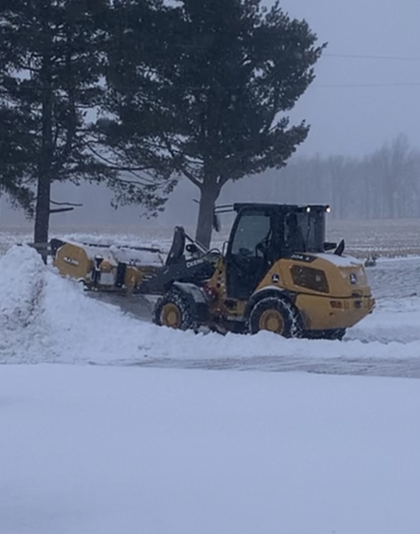 John Deere wheel loader with pusher box clearing snow in a rural lot during a snowstorm