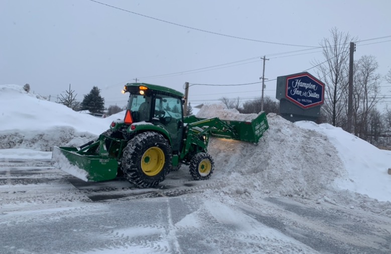 Green John Deere tractor with front loader clearing a commercial parking lot at Hampton Inn & Suites