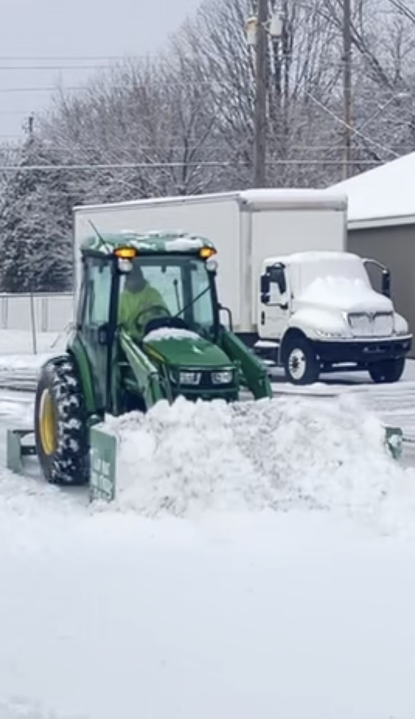 John Deere tractor with box plow pushing snow beside a box truck